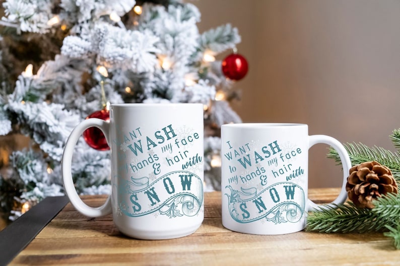 May include: Two white ceramic mugs with a winter-themed design. The mugs feature the text "I want to wash my hands & hair with snow" in blue lettering with a decorative snowflake design.