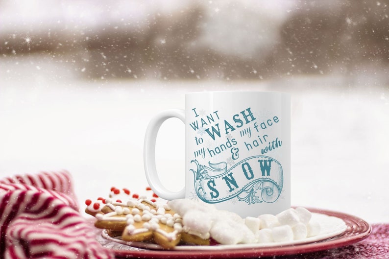 May include: White ceramic mug with a blue design that says "I want to wash my hands & hair with snow". The mug is sitting on a plate with marshmallows and gingerbread cookies.