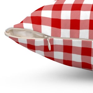 May include: A red and white checkered pillow with a zipper closure. The pillow has a classic picnic table pattern, with a close-up view of the fabric and zipper.