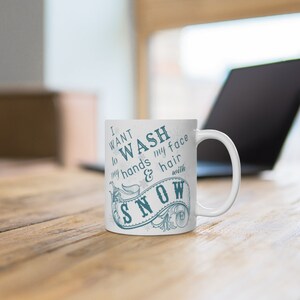 May include: White ceramic mug with a blue design that says "I want to wash my hands & hair with snow".