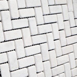 Op de afbeelding: Witte keramische tegelmozaïek in een visgraatpatroon. De tegels zijn rechthoekig en hebben een licht getextureerd oppervlak.