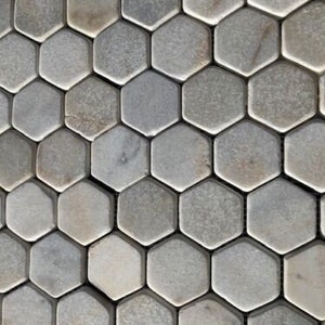 May include: Close-up of a mosaic tile pattern. The tiles are hexagonal, with a natural stone appearance. The color palette is primarily grey, with variations in tone and texture across the individual tiles. The overall effect is a neutral, organic design.