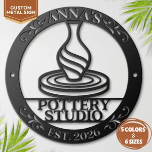 May include: A circular black metal sign featuring a cutout design of a vase on a pottery wheel. The text reads ANNA'S POTTERY STUDIO and EST. 2026. The sign includes decorative scrollwork along the inner border and two mounting holes on the sides.