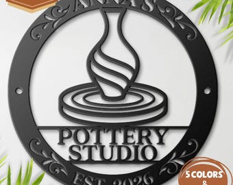 May include: A circular black metal sign featuring a cutout design of a vase on a pottery wheel. The text reads ANNA'S POTTERY STUDIO EST. 2026. The sign includes decorative scrollwork along the inner border and two mounting holes on the sides.