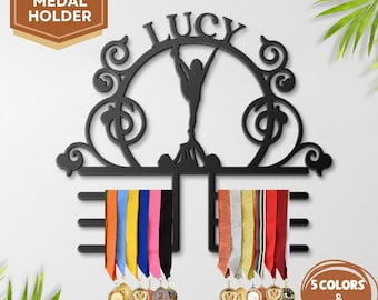 May include: A black metal medal holder featuring the name "LUCY" and a gymnast silhouette. The holder has two horizontal bars for displaying medals with colourful ribbons. The text "CUSTOM MEDAL HOLDER" is in the upper left corner.