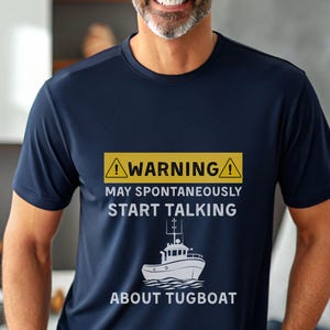 May include: Navy blue t-shirt with a humorous warning about talking about tugboats. The yellow and black warning sign is above the text "MAY SPONTANEOUSLY START TALKING ABOUT TUGBOAT" and a white illustration of a tugboat.