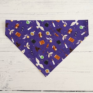 May include: Purple bandana with a repeating pattern of Harry Potter themed illustrations, including a golden snitch, a book, a wand, a potion bottle, and a Hogwarts house crest.
