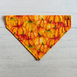 Op de afbeelding: Een driehoekige oranje en gele stoffen bandana met een pompoenprint.