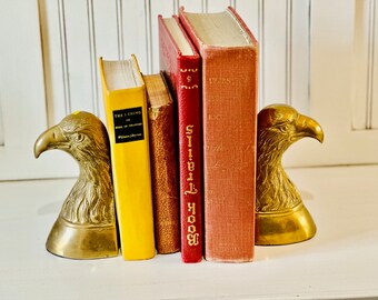 May include: A pair of gold eagle bookends holding up four books. The books are all hardback and have different colored covers. The book on the left has the title "The I Ching or Book of Changes" on the spine. The book on the right has the title "West" on the spine.