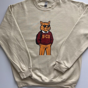 May include: A beige crewneck sweatshirt featuring a graphic illustration of an orange cat wearing sunglasses, a white collared shirt, and a maroon sweater with the text B-CU printed in yellow, paired with orange trousers and a black backpack.