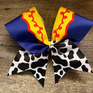 May include: A blue and yellow cheer bow with a red and yellow pattern on the top and a black and white cow print on the bottom.