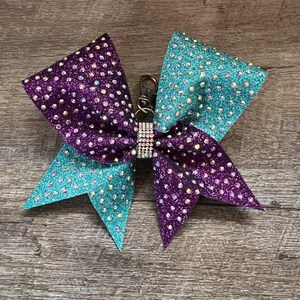 May include: A teal and purple cheer bow with rhinestones and a silver clip.