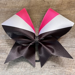 May include: A black cheer bow with pink and white stripes. The bow is tied with a black elastic band.
