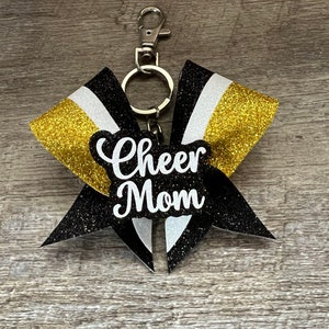 May include: Black, gold, and white glitter cheer bow with a silver key chain and the text "Cheer Mom" in white.