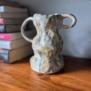 May include: A ceramic vase with two handles, featuring a textured, mottled glaze in shades of brown, green, and white.