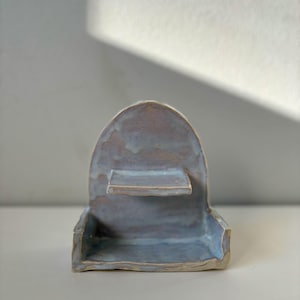 May include: A ceramic shelf with two levels, one on top of the other. The shelf is a light blue color with a white glaze. The shelf is shaped like an arch.