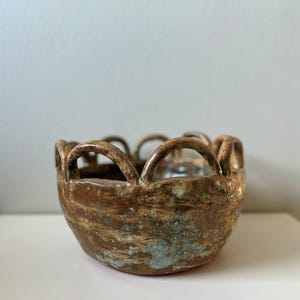 May include: A brown ceramic bowl with a scalloped rim. The bowl has a speckled glaze with blue and white accents.