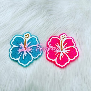 May include: Two colorful hibiscus flower shaped coasters. One is blue with white and gold accents, the other is pink with white and gold accents.