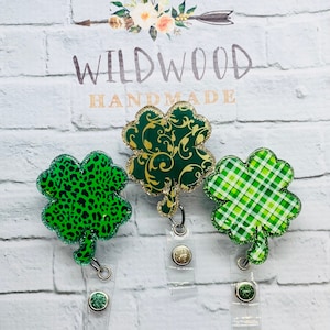 May include: Three shamrock-shaped badge reels in green with glitter accents. One has a leopard print, another has a gold floral design, and the third has a plaid pattern. The reels are attached to clear plastic holders.