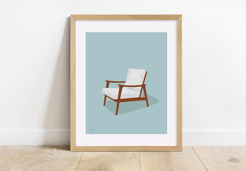 May include: A framed print featuring a mid-century modern armchair. The chair has a white cushion and backrest, with brown wooden arms and legs. The background is a light blue, and the frame is light brown.