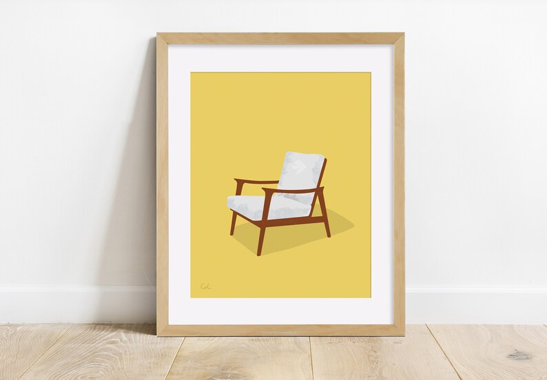 May include: A framed print featuring a mid-century modern armchair illustration. The chair has a white seat and back, brown wooden frame, and armrests. The background is a solid yellow, and the frame is light brown.