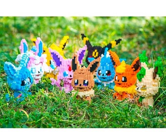 Könnte beinhalten: Eine Sammlung von neun bunten Pokémon-Charakteren aus Bausteinen. Die Figuren sind in einer Reihe auf einem Bett aus grünem Gras angeordnet. Die Figuren umfassen Eevee, Vaporeon, Jolteon, Flareon, Espeon, Umbreon, Leafeon, Glaceon und Sylveon.