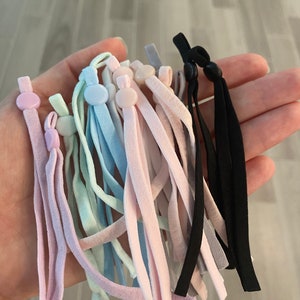 May include: A collection of colorful elastic mask extenders with adjustable buttons. The extenders are in various shades of pink, blue, and gray, with some black extenders.