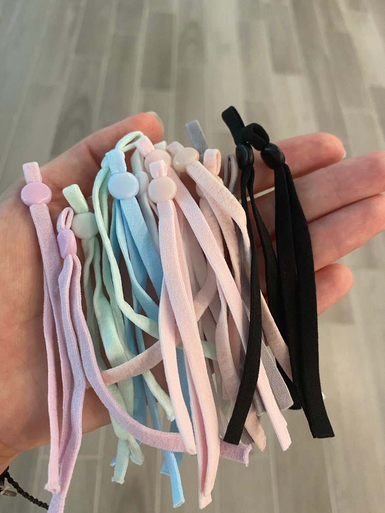 May include: A collection of colorful elastic mask extenders with adjustable buttons. The extenders are in various shades of pink, blue, and gray, with some black extenders.