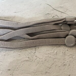 May include: A set of six gray elastic straps with gray plastic adjustable toggles. The straps are bundled together and the toggles are visible.