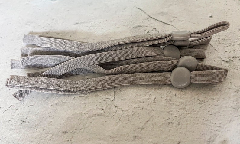 May include: A set of six gray elastic straps with gray plastic adjustable toggles. The straps are bundled together and the toggles are visible.