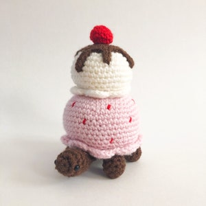 May include: A crocheted turtle wearing a pink and white ice cream cone with a red cherry on top.
