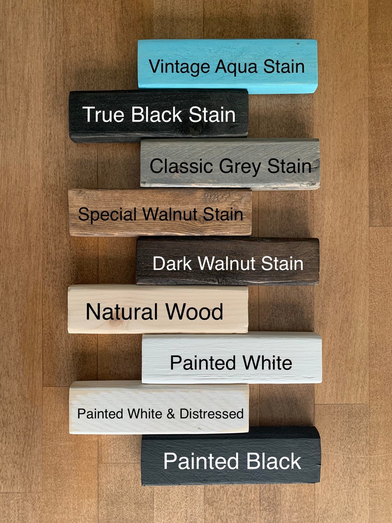 May include: Nine wooden blocks stacked on top of each other, each block has a different color and text. The colors are aqua, black, gray, brown, dark brown, natural wood, white, white with distressed paint, and black. The text on the blocks reads: Vintage Aqua Stain, True Black Stain, Classic Grey Stain, Special Walnut Stain, Dark Walnut Stain, Natural Wood, Painted White, Painted White & Distressed, Painted Black.