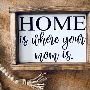 May include: A wooden framed sign with the text "HOME is where your mom is." in black lettering on a white background.