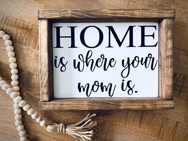 May include: A wooden framed sign with the text "HOME is where your mom is." in black lettering on a white background.