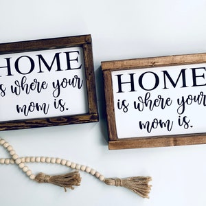 May include: Two wooden signs with the text "HOME is where your mom is." in black lettering on a white background.
