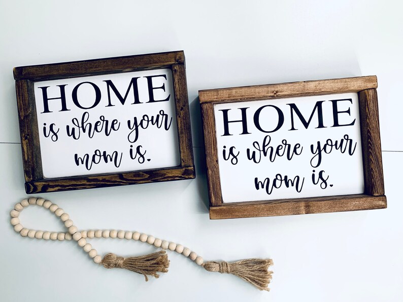 May include: Two wooden signs with the text "HOME is where your mom is." in black lettering on a white background.