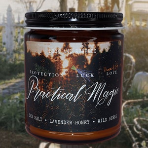 May include: A glass jar candle with a black lid and a label that reads "Practical Magic." The label features a forest scene with the words "Protection, Luck, Love" and the ingredients "Sea Salt, Lavender Honey, Wild Herbs."