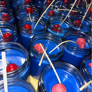 May include: A collection of blue-colored candles in glass jars, each with a red skull-shaped decoration and a white wick. The candles are arranged closely together, creating a visually striking display. The blue wax contrasts with the red skulls.
