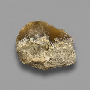 May include: A rough, irregularly shaped stone fragment featuring a translucent, amber-colored upper section and a textured, opaque beige base. The surface displays natural fractures and sharp, jagged edges characteristic of raw flint or chert material.