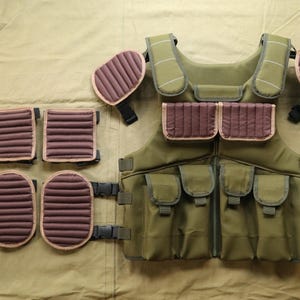 May include: Olive green tactical vest with multiple pockets and brown padded sections. Includes shoulder pads, chest pockets, and lower leg protection. Features adjustable straps and buckles for a secure fit. Designed for protection and utility.