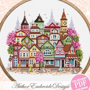 May include: Cross stitch pattern of a colourful town with houses, trees, and Easter eggs. The pattern is in a round embroidery hoop and is labelled "Author Embroide Design" and "cross stitch pattern PDF instant download".