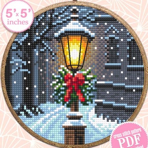 May include: A cross stitch pattern PDF for a 5x5 inch embroidery hoop featuring a snowy winter scene with a lit street lamp decorated with a red bow and green garland.