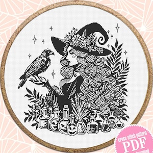May include: Black and white cross stitch pattern of a witch with a raven, flowers, and potion bottles. The pattern is in a round embroidery hoop.