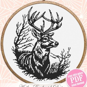 Puede incluir: Patrón de punto de cruz en blanco y negro de un ciervo con grandes cuernos en un entorno de bosque. El patrón está enmarcado en un aro de madera. El texto "cross stitch pattern PDF instant download" está en un círculo rosa.
