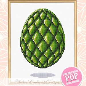 May include: A framed cross-stitch pattern featuring a green, textured egg design. The egg has a scale-like pattern and is set against a white background. The frame is a light wood color. The image includes the text "Author Embroide Design" and "Cross stitch pattern PDF instant download".