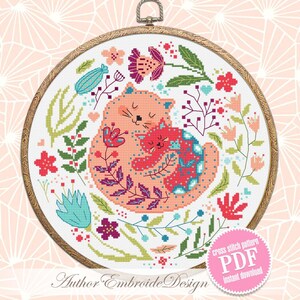 May include: Cross stitch pattern PDF for a colorful embroidery design of two cats cuddling surrounded by flowers. The design features a pink and red cat with a smaller red cat nestled inside. The background is a white circle with a variety of flowers in shades of pink, red, blue, green, and purple.