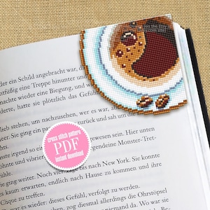 Op de afbeelding: Een pagina uit een boek met een kruissteek-bladwijzer met een kopje koffie en twee bruine suikerklontjes. Een roze en witte cirkel met de tekst "cross stitch pattern PDF instant download" is zichtbaar.