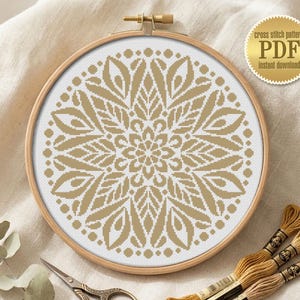 May include: A circular wooden embroidery hoop containing a white fabric with a gold-colored geometric mandala cross stitch pattern. Beside the hoop are metal scissors and three skeins of gold embroidery floss. A gold circular badge reads cross stitch pattern PDF instant download.