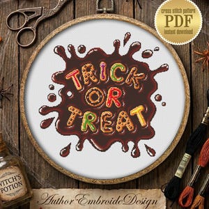 Könnte beinhalten: Ein Halloween-Kreuzstichmuster in einem Holzrahmen. Das Design zeigt die Worte "Trick or Treat" in bunten, keksartigen Buchstaben auf einem schokoladenfarbenen Hintergrund. Das Bild enthält Kürbisse, Spinnen und Herbstblätter.