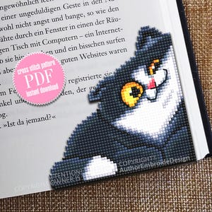 Peut inclure: Un chat noir et blanc aux yeux jaunes se cache derrière un livre. Le livre contient du texte en allemand et un cercle rose avec les mots "cross stitch pattern PDF instant download".